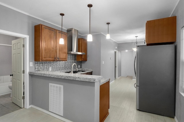 kitchen with visible vents, brown cabinetry, wall chimney exhaust hood, freestanding refrigerator, and a peninsula