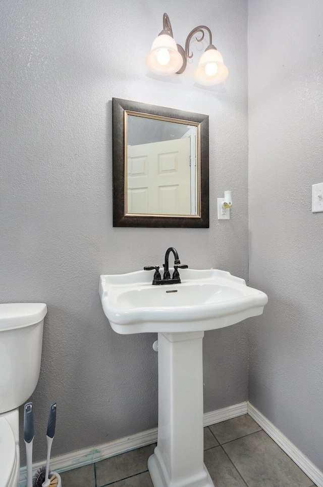 half bathroom with toilet, baseboards, a sink, and tile patterned floors