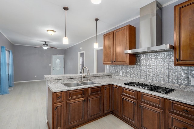 kitchen with stainless steel gas cooktop, a sink, light countertops, wall chimney range hood, and decorative backsplash