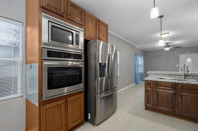 kitchen with ceiling fan, light wood-style flooring, stainless steel appliances, a sink, and hanging light fixtures