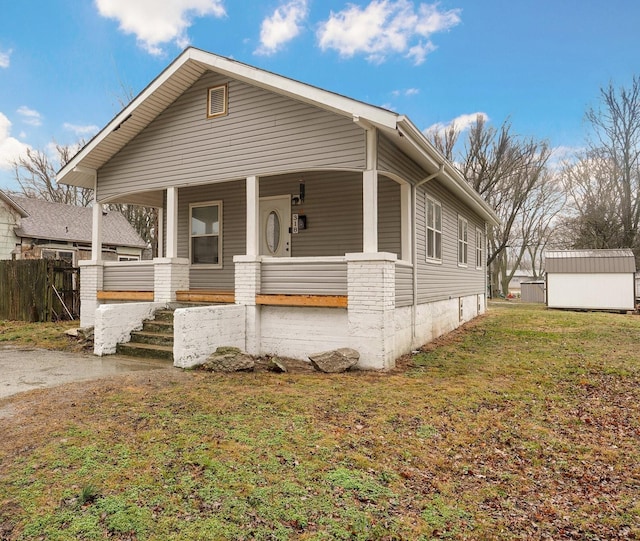 bungalow with a storage shed, covered porch, fence, an outdoor structure, and a front yard