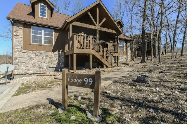 view of front of home with board and batten siding, stone siding, a shingled roof, and stairs