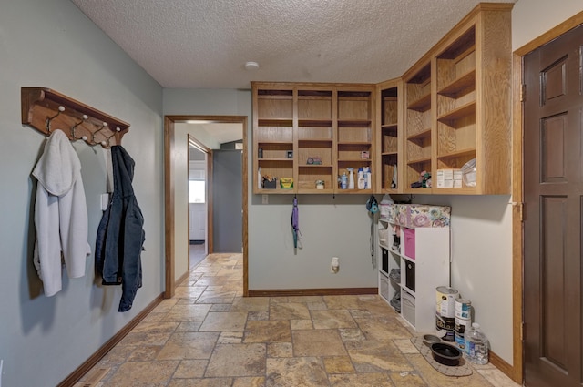 mudroom with baseboards, a textured ceiling, and stone tile floors