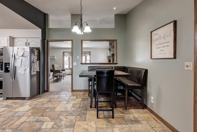 dining room featuring a notable chandelier, a textured ceiling, stone tile flooring, and baseboards