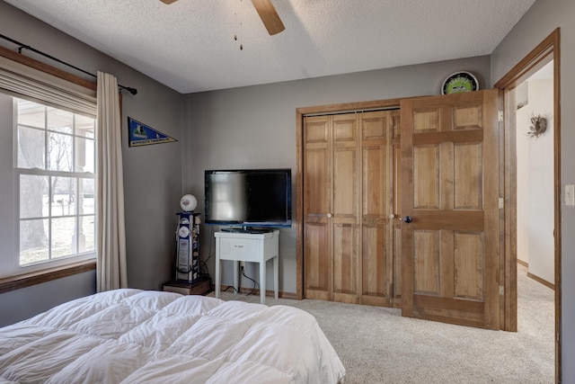 carpeted bedroom with ceiling fan, a textured ceiling, baseboards, and a closet