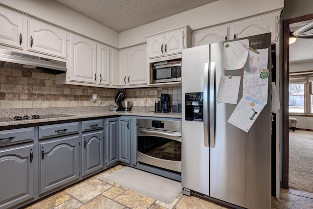 kitchen with a textured ceiling, under cabinet range hood, stainless steel appliances, white cabinets, and gray cabinets