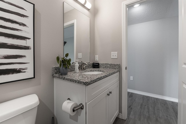 bathroom featuring baseboards, vanity, toilet, and wood finished floors