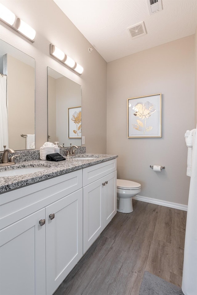 full bath with toilet, visible vents, a sink, and wood finished floors