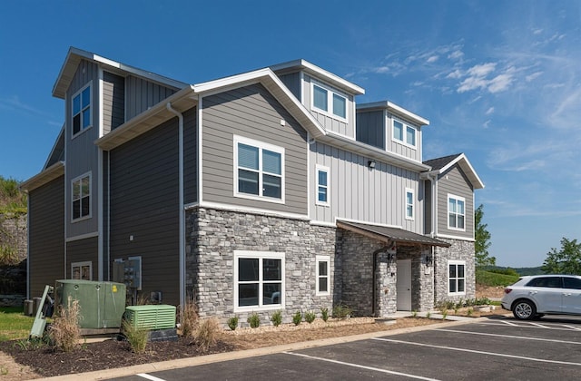 view of front of home with board and batten siding, stone siding, and uncovered parking