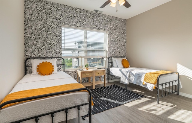 bedroom featuring visible vents, an accent wall, a ceiling fan, wood finished floors, and baseboards