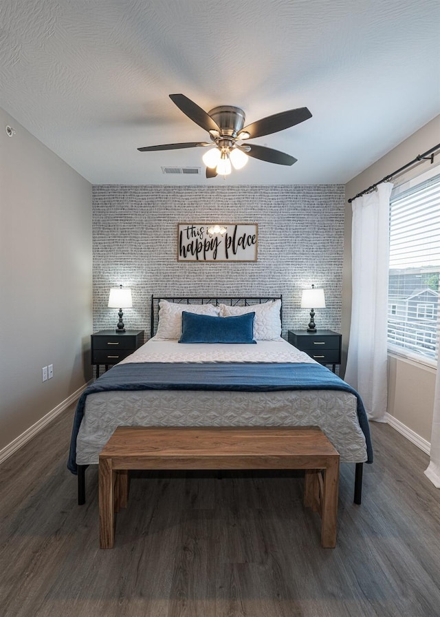 bedroom featuring baseboards, an accent wall, visible vents, and wood finished floors