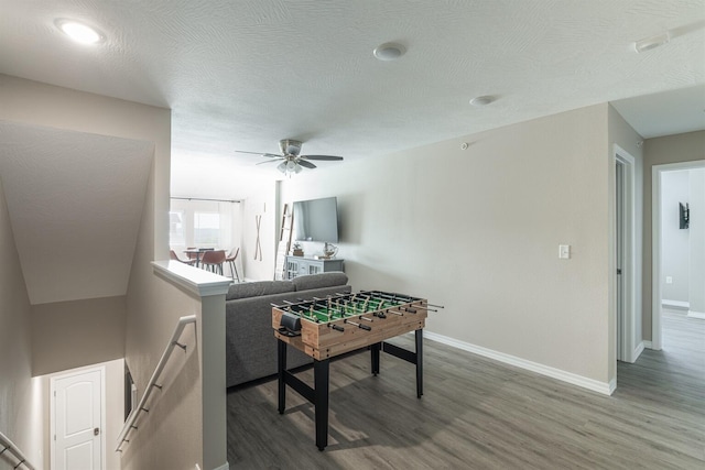 rec room featuring a textured ceiling, wood finished floors, a ceiling fan, and baseboards