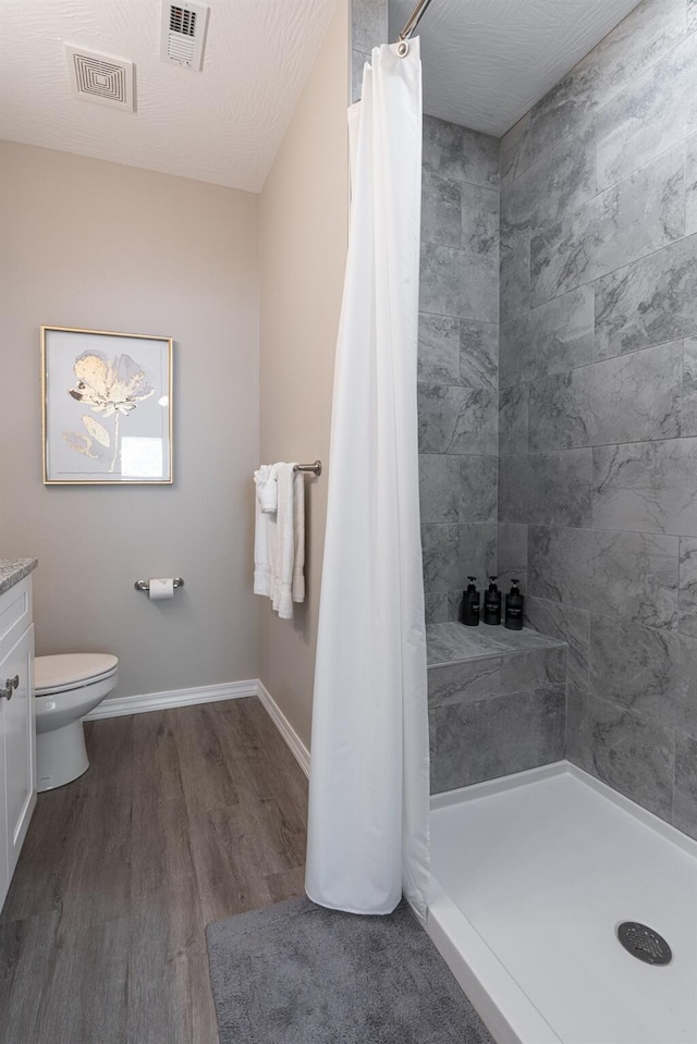 bathroom featuring toilet, wood finished floors, visible vents, and a shower stall