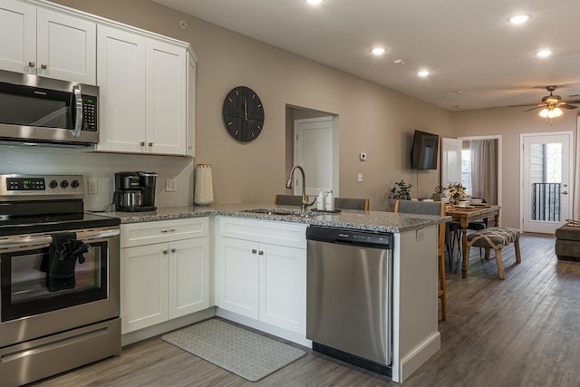 kitchen featuring a peninsula, stainless steel appliances, light wood-type flooring, white cabinetry, and a sink