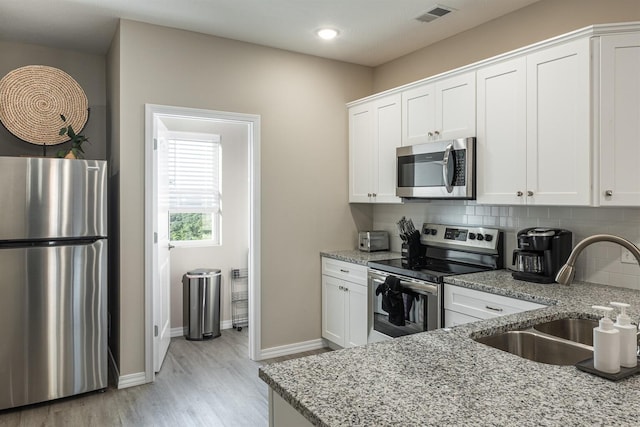 kitchen with stainless steel appliances, tasteful backsplash, visible vents, a sink, and light stone countertops