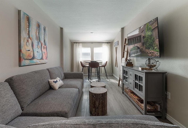 living room featuring baseboards, light wood-style flooring, and a textured ceiling