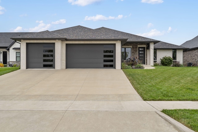 prairie-style house with a garage, a front lawn, a shingled roof, and brick siding