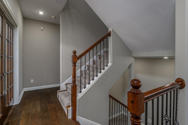 staircase featuring a textured ceiling, wood finished floors, and baseboards