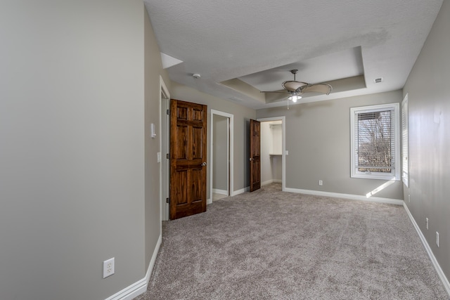 unfurnished bedroom with baseboards, a raised ceiling, ceiling fan, a walk in closet, and carpet flooring