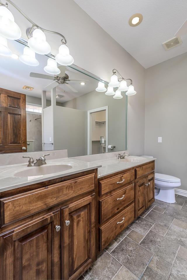 full bath featuring toilet, stone tile flooring, a sink, and visible vents