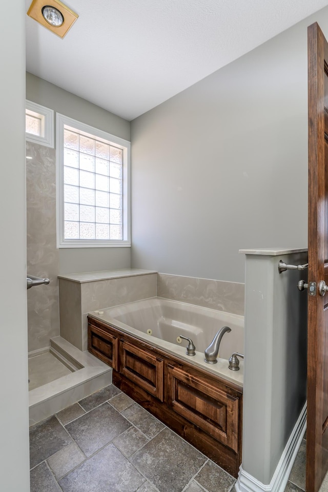 bathroom featuring a tub with jets, a shower, and stone tile flooring