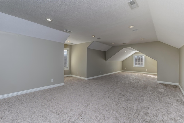 additional living space with carpet floors, visible vents, vaulted ceiling, a textured ceiling, and baseboards