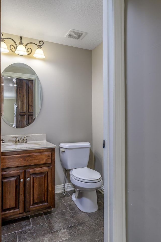 bathroom with toilet, visible vents, vanity, baseboards, and stone finish flooring