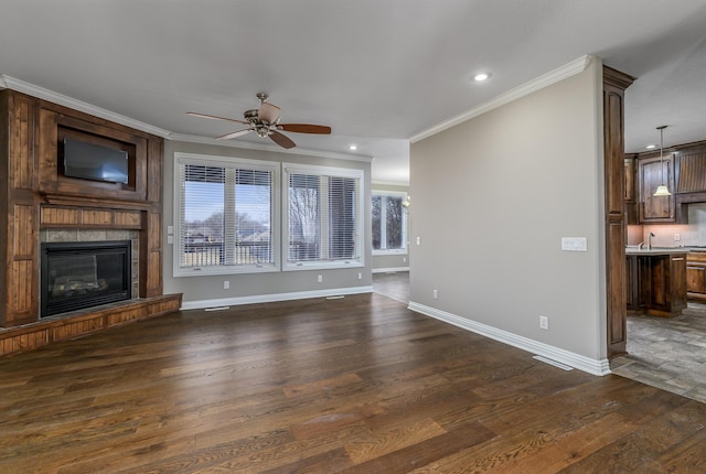 unfurnished living room featuring ceiling fan, a large fireplace, baseboards, ornamental molding, and dark wood finished floors