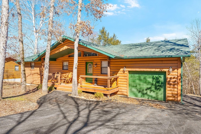 cabin with aphalt driveway, faux log siding, covered porch, and an attached garage