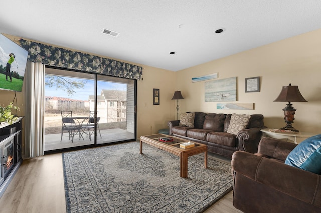 living room with light wood-type flooring, visible vents, and a textured ceiling