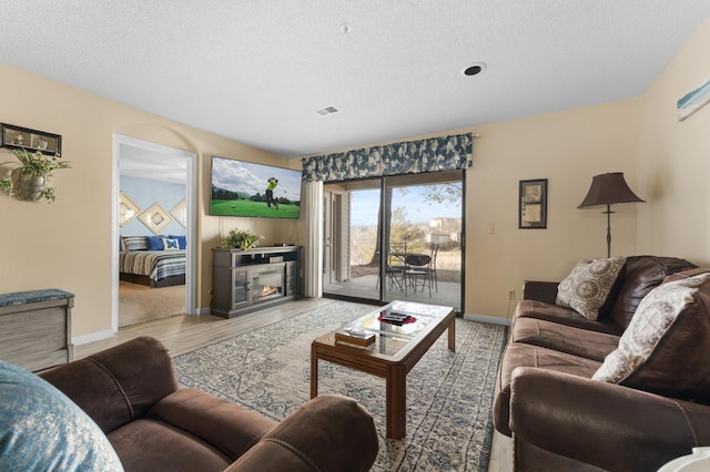 living room with a textured ceiling, wood finished floors, a glass covered fireplace, and visible vents