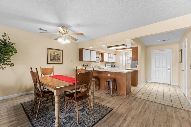 dining room featuring visible vents, light wood-style flooring, ceiling fan, a textured ceiling, and baseboards