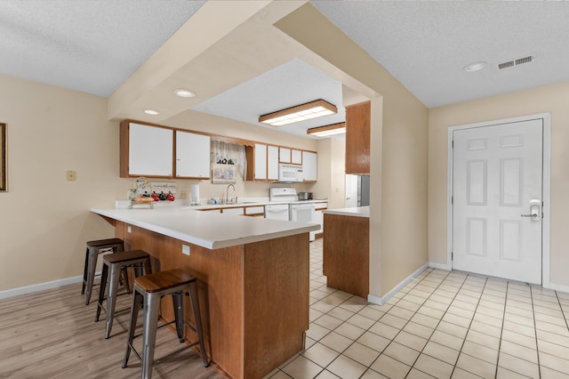 kitchen featuring light countertops, visible vents, a sink, white appliances, and a peninsula