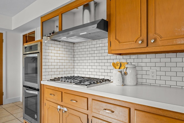 kitchen with light tile patterned floors, stainless steel appliances, light countertops, wall chimney range hood, and backsplash