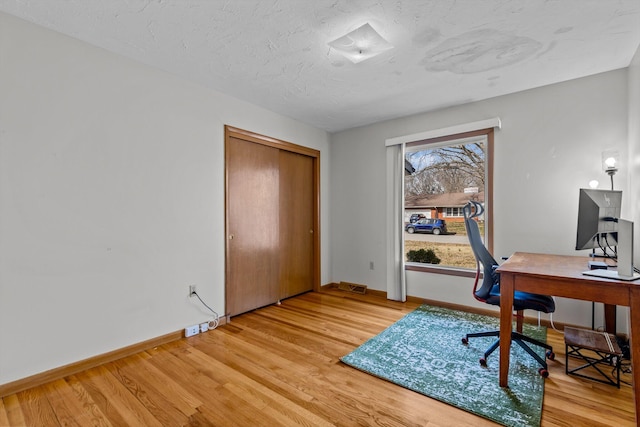 office space with light wood-style floors, a textured ceiling, and baseboards