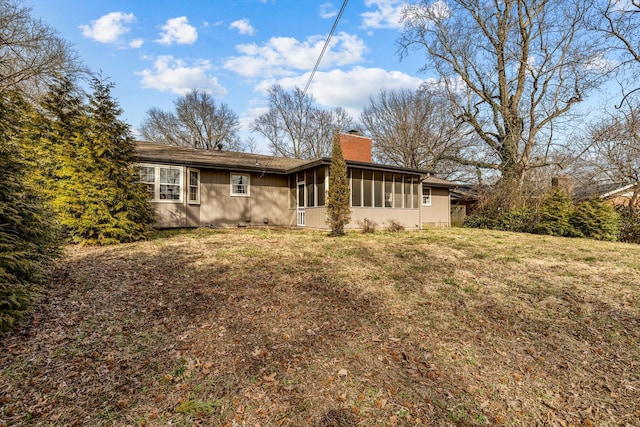 rear view of house with a sunroom, a lawn, and a chimney