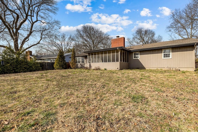 back of property featuring a sunroom, a chimney, fence, and a lawn