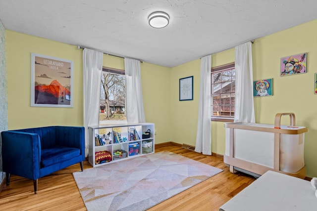 sitting room featuring baseboards, wood finished floors, visible vents, and a healthy amount of sunlight