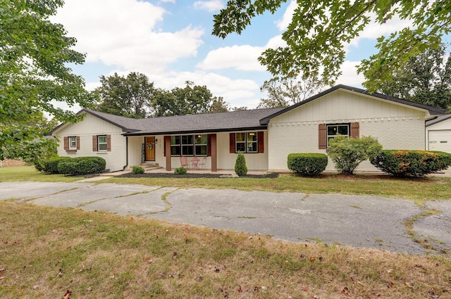 single story home featuring covered porch, brick siding, and a front yard