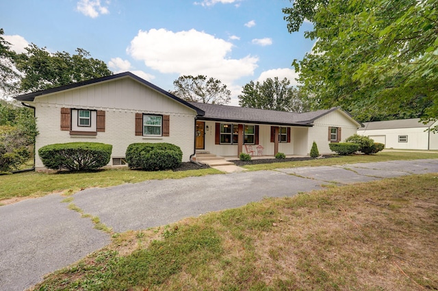 single story home featuring a porch, a front yard, aphalt driveway, and brick siding