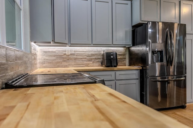 kitchen with tasteful backsplash, butcher block counters, gray cabinetry, and stainless steel fridge with ice dispenser