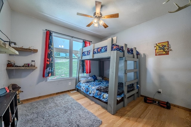 bedroom with a ceiling fan, a textured ceiling, baseboards, and wood finished floors