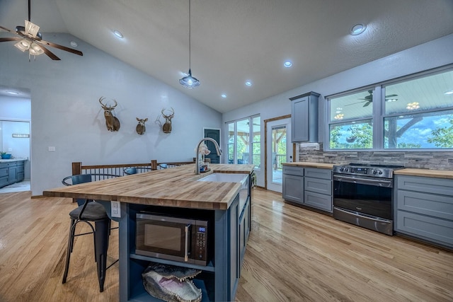 kitchen with light wood-style flooring, ceiling fan, stainless steel appliances, gray cabinetry, and wooden counters