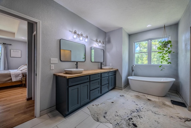 full bathroom with a textured ceiling, a sink, baseboards, a soaking tub, and double vanity