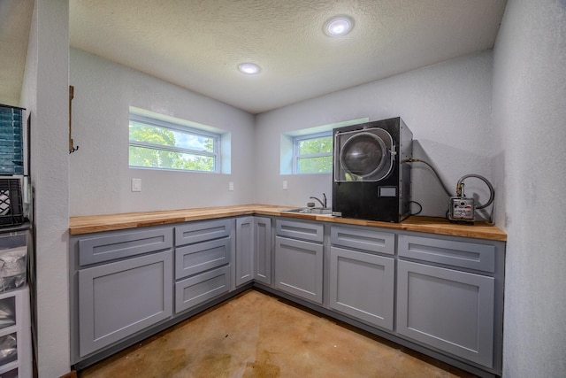 kitchen with a sink, butcher block counters, concrete floors, and gray cabinets