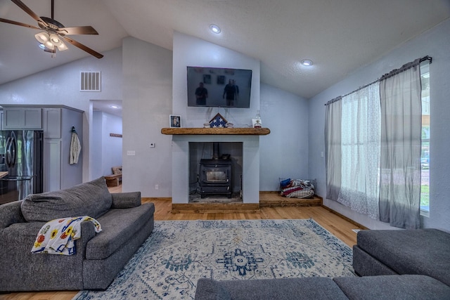 living area featuring lofted ceiling, ceiling fan, wood finished floors, visible vents, and a wood stove