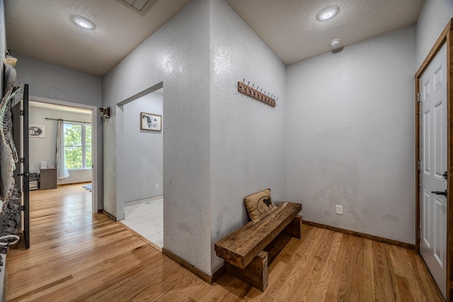 hall with a textured ceiling, a textured wall, and wood finished floors