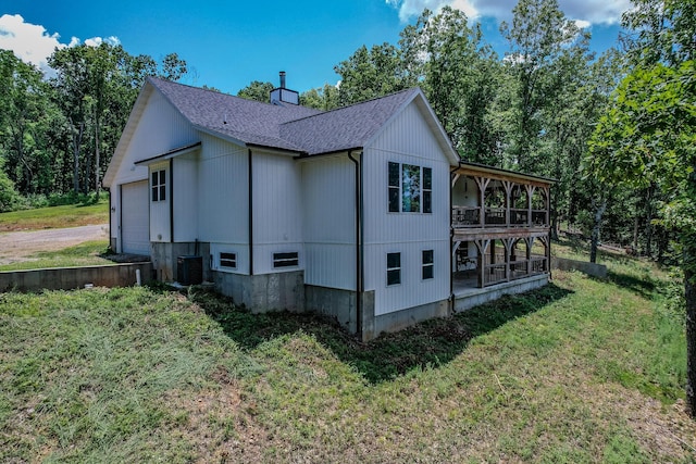 view of side of home featuring a garage, a shingled roof, a lawn, and central AC unit