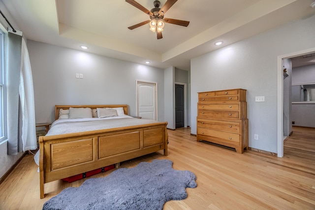 bedroom with a tray ceiling, recessed lighting, light wood-style floors, ceiling fan, and baseboards