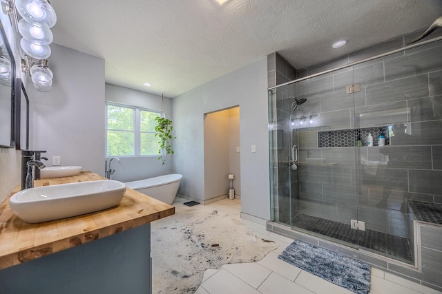 bathroom featuring a textured ceiling, a sink, a shower stall, tile patterned floors, and double vanity